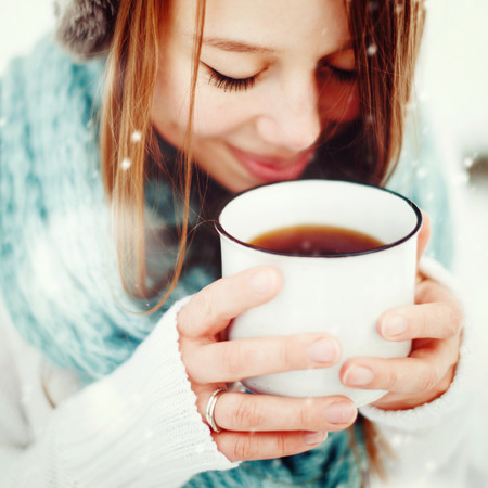 Young Beautiful Female Drinking Hot Drink Outdoors in Winter. Close Up Headshot. Drawn Snow. Selective Focus.の写真素材