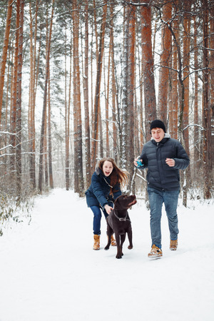 Young Couple with a Dog Having Fun in Winter Forest on Vacations. Selective Focus. Lifestyle of Happy Modern Family.の写真素材