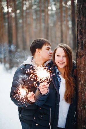 Happy Couple Celebrating Christmas in Winter Forest with Sparklers. Romantic Evening. Selective Focus on Woman.の写真素材
