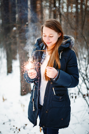 Beautiful Smiling Female in Warm Clothing Holding Sparklers in Winter Forest. Festive Mood.の写真素材