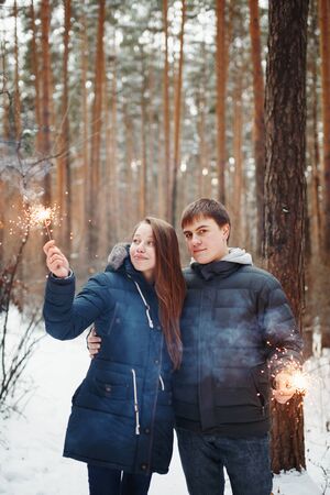 Young Family Standing in a Winter Forest with Sparklers for Festive Moodの写真素材