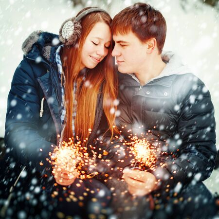 Happy Smiling Couple with Holiday Sparklers Celebrating Christmas Outdoors in Winter Forestの写真素材