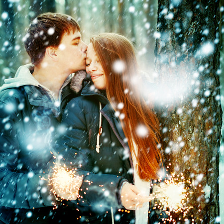 Beautiful Modern Couple in a Winter Forest with Sparklers for Festive Mood. Man Kissing Woman, Woman Smiling. Selective Focus. Close Up Portrait.の写真素材