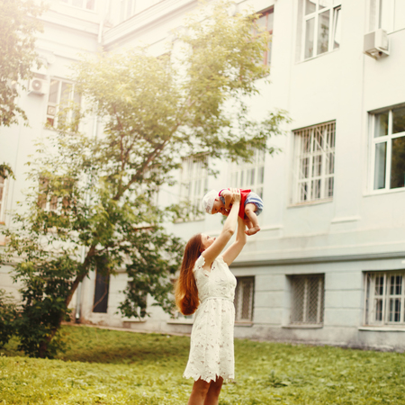 Young Happy Mother in White Dress Holding Her Baby Overhead. Selective Focus. Summer Time. Space For Text. Image Toned.の写真素材