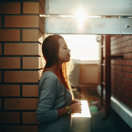 Young Woman Standing on a Street with Closed Eyes in Sunset Light. Selective Focus, Lens Flare.の写真素材
