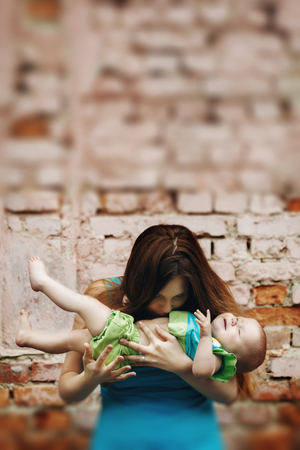 Portrait of Loving Young Mother Holding and Kissing Her Baby against Brick Wall. Selective Focus, Tilt Shift Blurred Effect Added.の写真素材