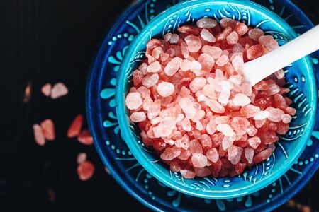 Himalayan Pink Salt Crystals Close Up in a Blue Ceramic Authentic Bowl on a Dark Wooden Surface. Top View, Selective Focus. Space for Text.の写真素材