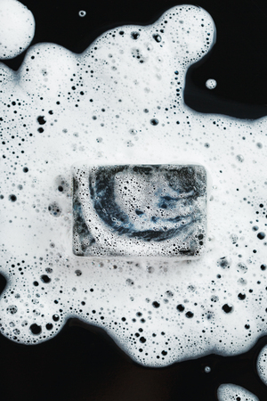 Black coal soap in foam on black background. Close-up composition. Top view.の写真素材
