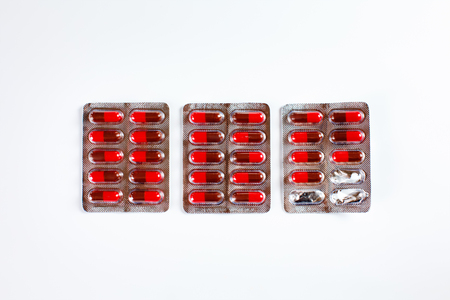 Row of blisters with red gelatin capsules, new and opened. View from above.の写真素材