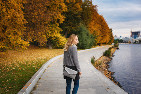 Woman walking in autumn park. Pensive and dreaming. Urban park scene. Embankment near river.の写真素材
