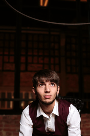 Modern portrait of brutal bearded man sitting on a chair in loft interior. Expressive emotions. Copy space, selective focus.の写真素材