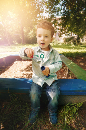 Cute little boy playing at the children playground outdoors with soap bubbles. Lens flare effect.の写真素材