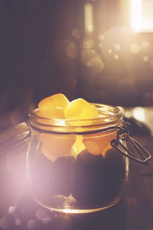 Mason jar full of jelly candies in sunset illuminated kitchen with bokeh light effect. Selective focus, image toned.の写真素材