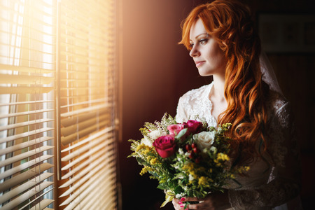 Wedding portrait. Beautiful bridal with flower bouquet standing near window. Headshot composition.の写真素材