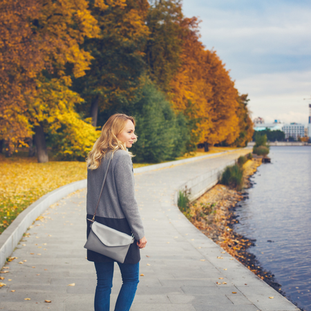 Woman walking in autumn park. Pensive and dreaming. City park scene. Embankment near river. Vintage colors.の写真素材