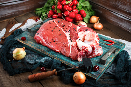 Fresh beef veal meat on rustic wooden table with kitchen utensils and vegetables, rustic styleの写真素材