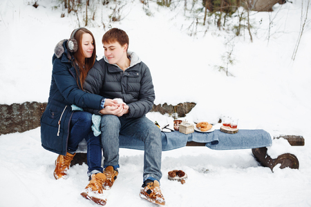 Couple in love drinking hot tea outside, winter forest with wooden house at the backgroundの写真素材