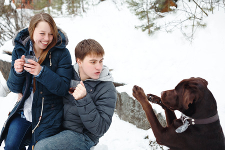 Couple drinking hot drink outdoors in rural winter weekend, funny labrador dog asking a cookieの写真素材