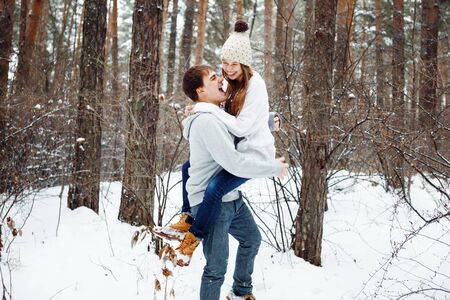 Couple in love having fun, winter forest at the background, man holding womanの写真素材