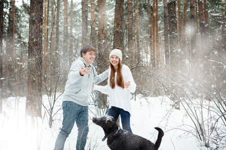 Young funny couple having fun in snowy forest with dogの写真素材