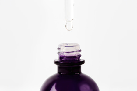 Essential oil or serum dropping from pipette to the bottle with liquid cosmetic product, white background, selective focusの写真素材