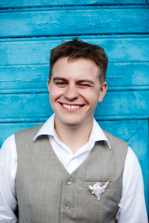 Handsome young man in grey suite smiling and  posing against blie backgroundの写真素材