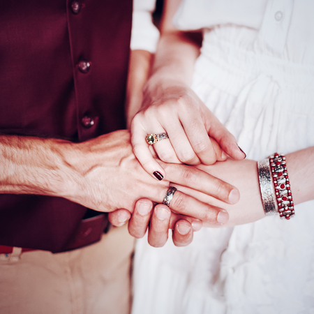 Male and female holding hands. Hands with boho chic accessories close-up. Wedding couple.の写真素材