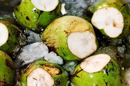 Fresh unpeeled coconuts in ice, fruit market in Thailandの写真素材