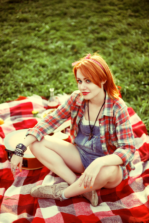 Young redhead hipster woman on the picnic, sitting on a plaidの写真素材