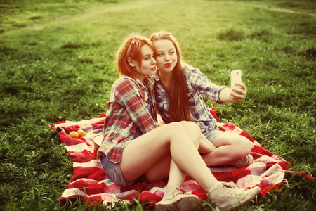 Two young hipster girls having fun on the picnic, making selfie on a smartphoneの写真素材