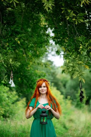 Red hair woman holding lantern, beautiful woman posing at the natureの写真素材