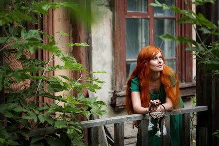 Young beautiful red hair woman posing in abandoned place among treesの写真素材