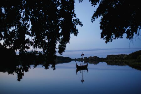 Evening background with lonely ship on the mirror water surface of lakeの写真素材