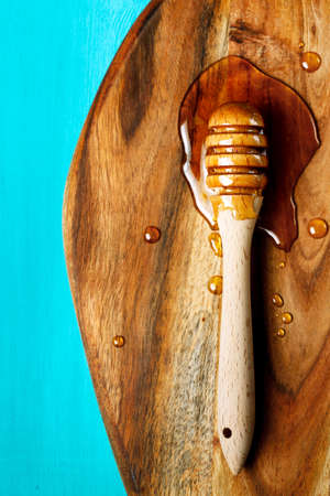 Honey spoon, special wooden dipper for liquid honey product close-up on a chopping board on a blue backgroundの写真素材