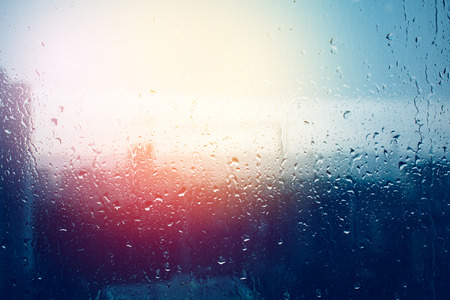 Raindrops on window glass surface, blurred city through window glass after rainの写真素材