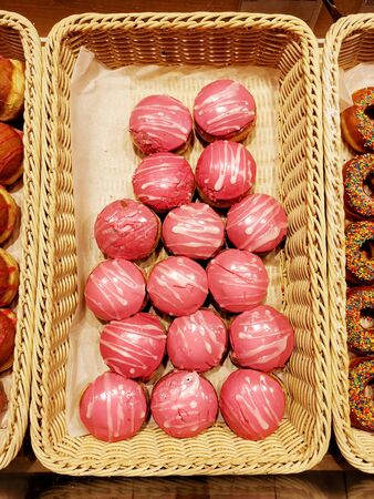 Sweet donuts with pink icing, pastries in basket in bakery shop, top viewの写真素材