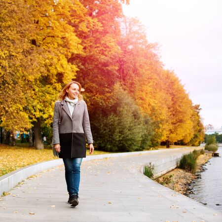 Elegant confident woman walking along the river in city park and smiling, sunny dayの写真素材