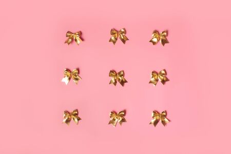Pink celebration background with golden bows. Festive present concept, flat lay.の写真素材