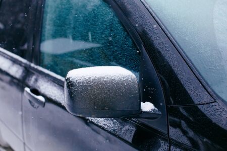 Close-up of side mirror of snow covered blue car parked outside, winter snowy weather conceptの写真素材