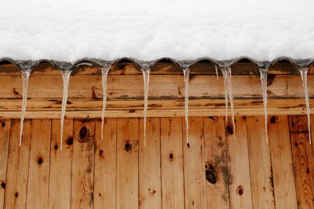 Row of icicles on the snowy roof of wooden buliding of a houseの写真素材