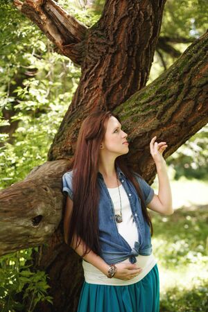 Young beautiful pregnant woman standing near tree outdoorsの写真素材