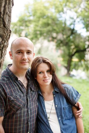 Beautiful young family, man and pregnant woman, embracing in park outdoors, close-upの写真素材