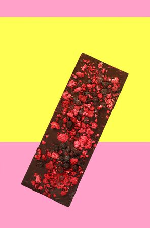 Chocolate with dried red berries on bright pink yellow background, top view