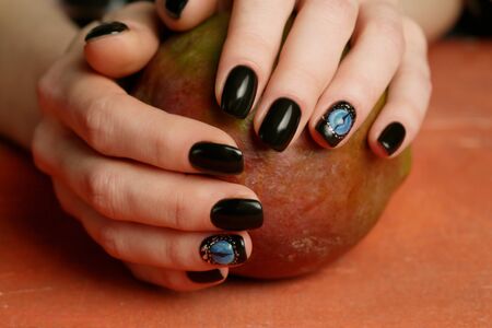 Dark nail art on manicured hands on red background close-up