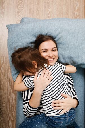 Beautiful smiling mother hugging her cute little daughter, mom and girl in same clothes lying. Top view.の写真素材