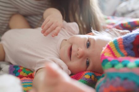 Close-up portrait of cute little baby lying on bed in morning light and smiling, just woke up, side...