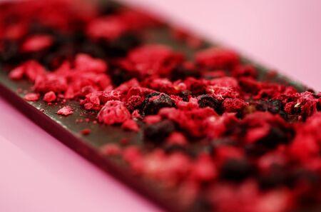 Dark low calorie chocolate with dried red berries on bright pink background, selective focus