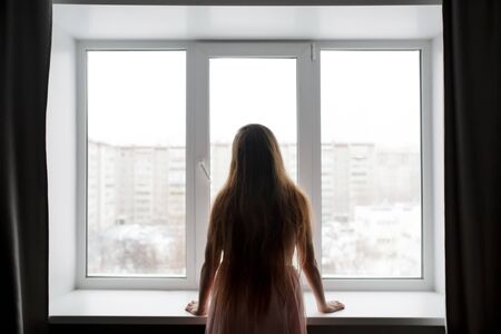 Rear view of woman silhouette standing near window looking out, melancholy and crisis conceptの写真素材