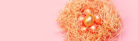 Happy easter background, colored pink and golden eggs in hay nest over bright pink color, top view...