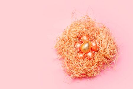 Happy easter background, colored pink and golden eggs in hay nest over bright pink color, top view with copy spaceの写真素材